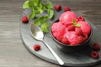 Photo of Delicious raspberry sorbet in bowl, fresh berries, mint and spoon on wooden table, closeup