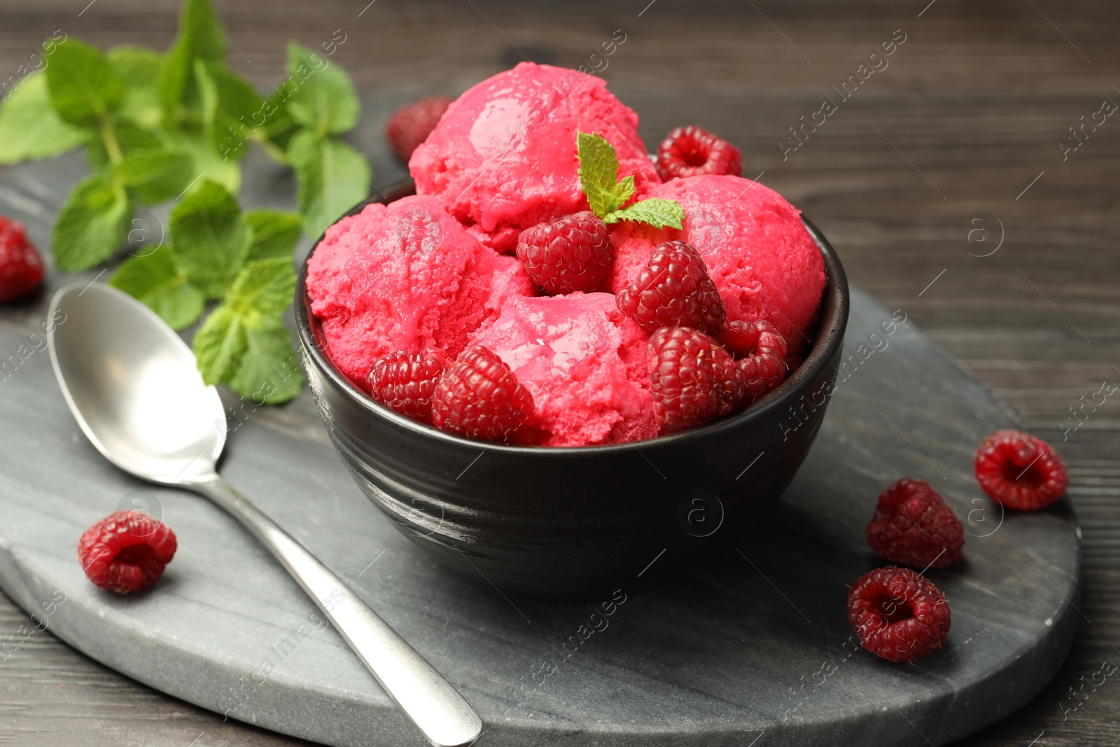 Photo of Delicious raspberry sorbet in bowl, fresh berries, mint and spoon on wooden table, closeup