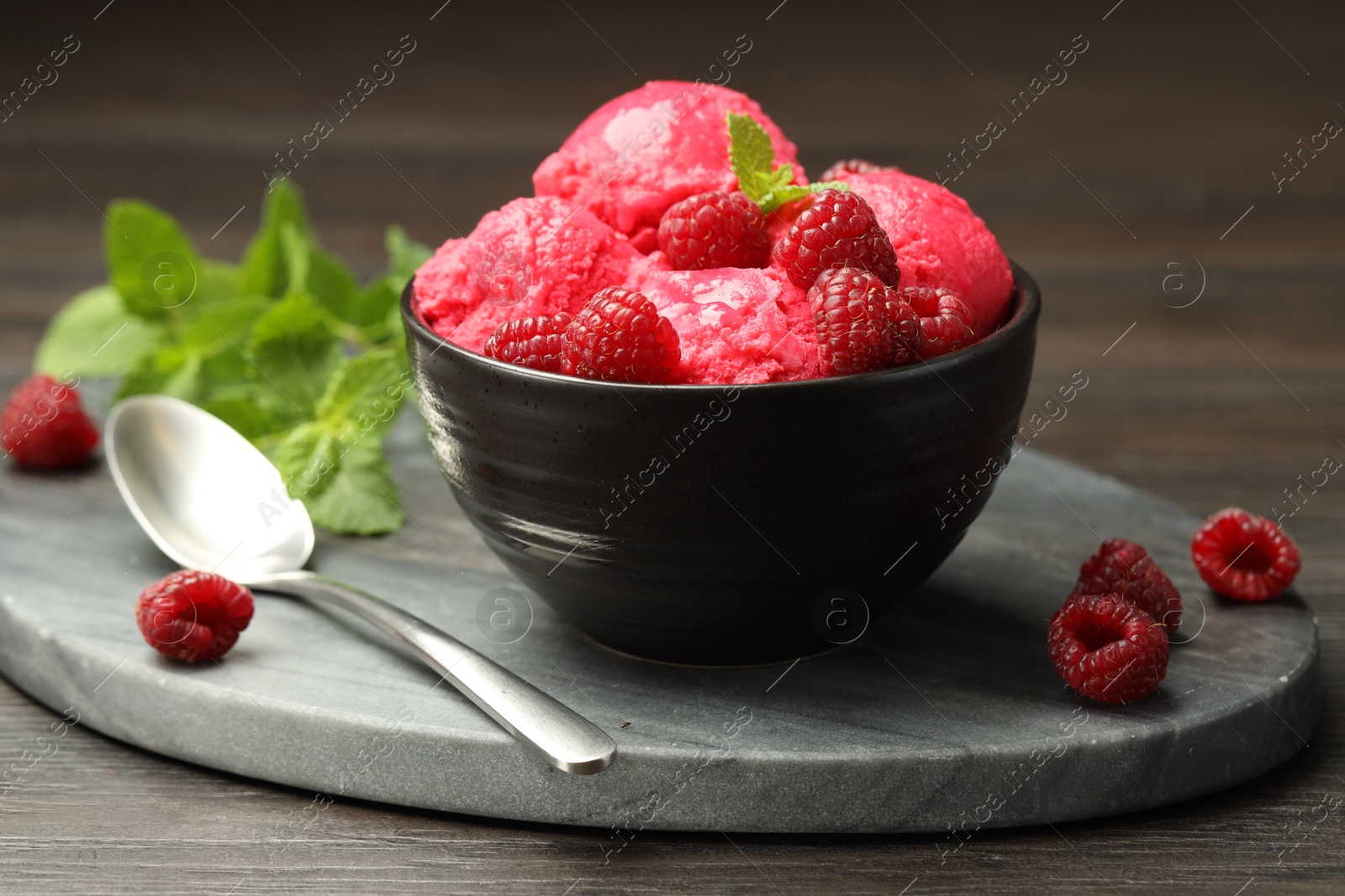 Photo of Delicious raspberry sorbet in bowl, fresh berries, mint and spoon on wooden table, closeup