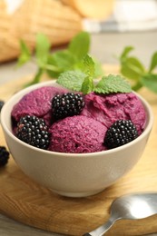 Photo of Delicious blackberry sorbet with fresh berries in bowl and spoon on table, closeup