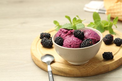 Photo of Delicious blackberry sorbet with fresh berries in bowl and spoon on wooden table