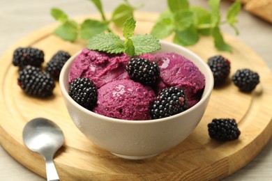 Photo of Delicious blackberry sorbet with fresh berries in bowl and spoon on table, closeup