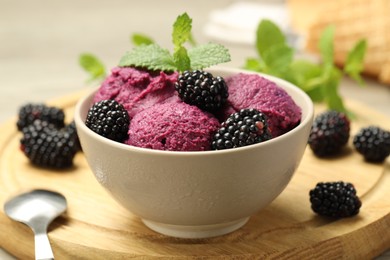 Photo of Delicious blackberry sorbet with fresh berries in bowl and spoon on table, closeup