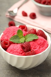 Photo of Delicious raspberry sorbet, fresh berries and mint in bowl on gray textured table, closeup