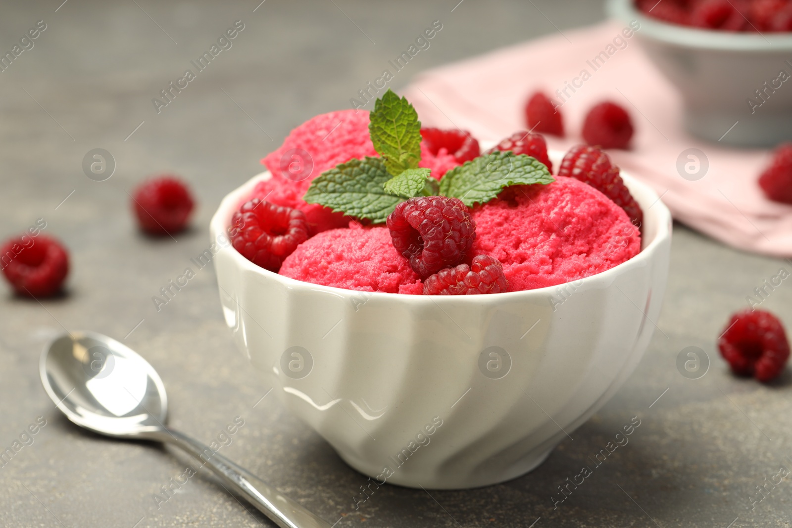 Photo of Delicious raspberry sorbet with fresh berries in bowl and spoon on gray textured table, closeup