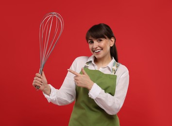 Happy pastry chef pointing at big whisk on red background