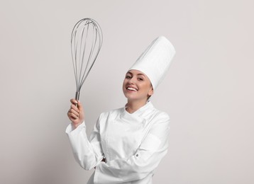 Happy pastry chef with big whisk on light grey background