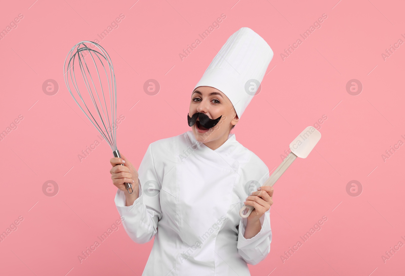 Image of Funny pastry chef with fake mustache holding big whisk and spatula on pink background