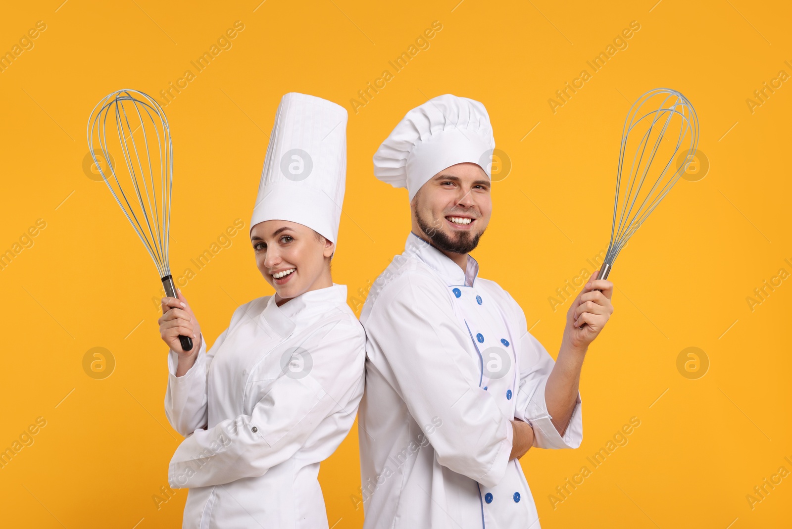 Image of Happy pastry chefs with big whisks on orange background