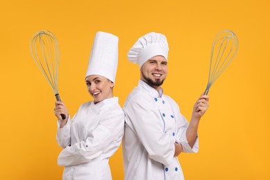 Happy pastry chefs with big whisks on orange background