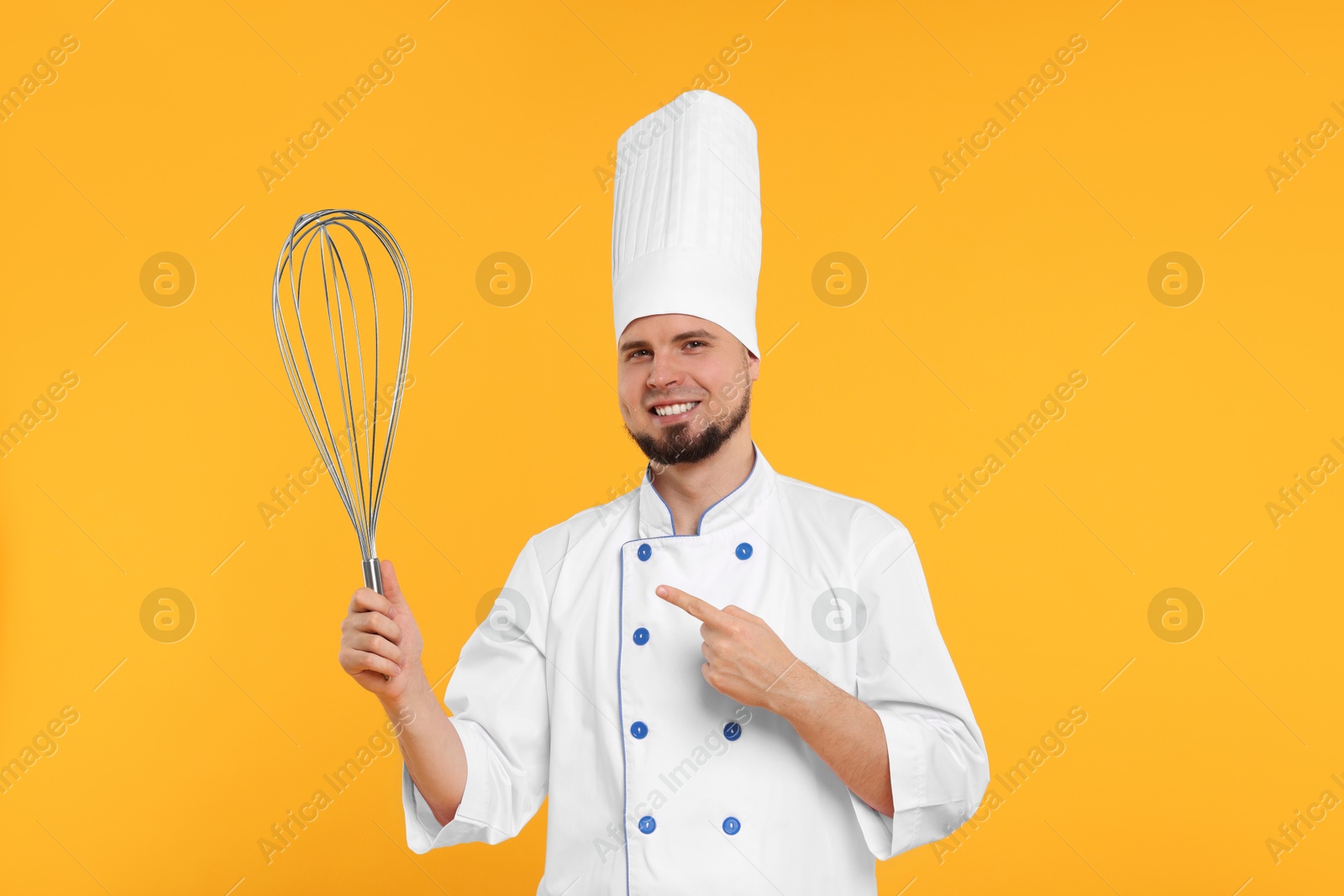 Image of Happy pastry chef pointing at big whisk on orange background