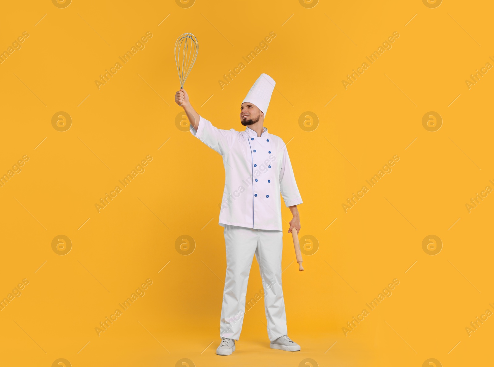 Image of Happy pastry chef with big whisk and rolling pin on orange background