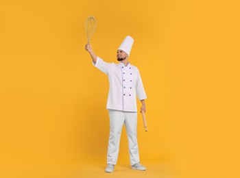 Image of Happy pastry chef with big whisk and rolling pin on orange background