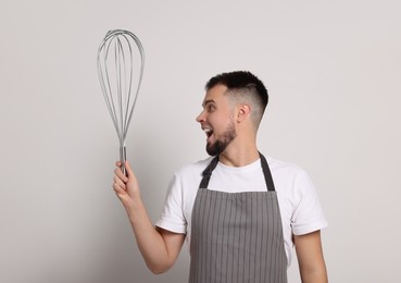 Emotional pastry chef with big whisk on light grey background