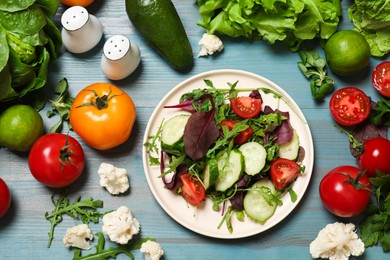 Photo of Healthy vegetarian food. Plate of salad and vegetables on light blue wooden table, flat lay