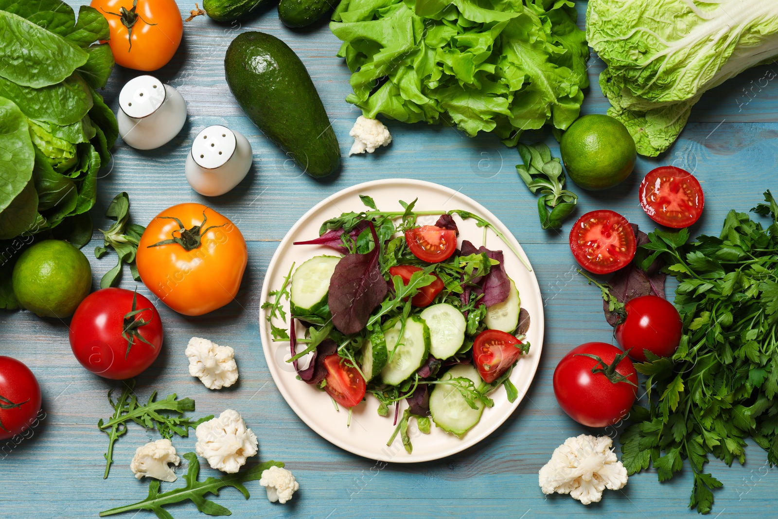 Photo of Healthy vegetarian food. Plate of salad and vegetables on light blue wooden table, flat lay