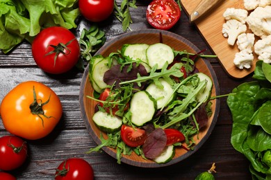 Photo of Healthy vegetarian food. Salad in bowl and vegetables on wooden table, flat lay