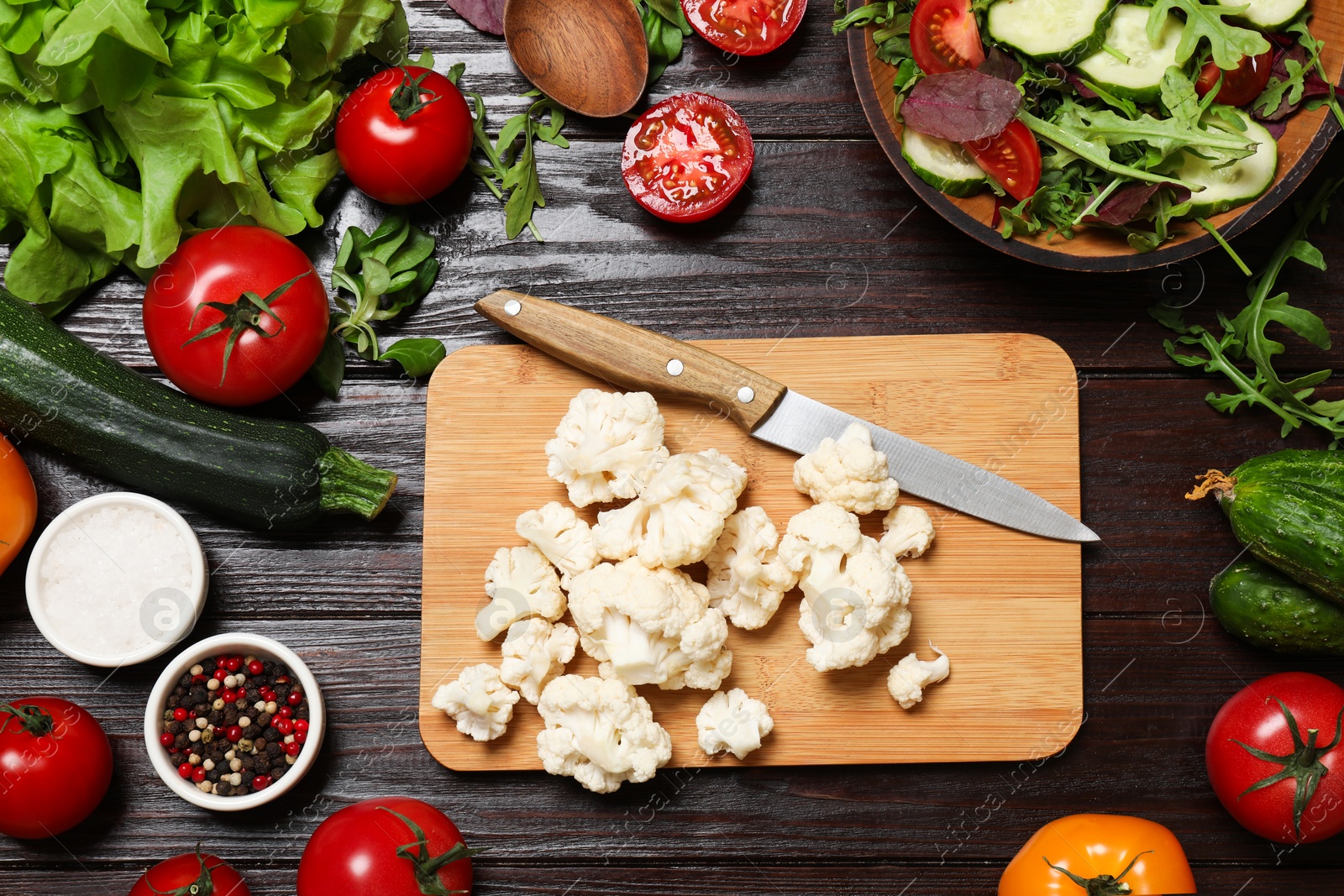 Photo of Healthy vegetarian food. Pieces of cauliflower, salad, peppercorns and vegetables on wooden table, flat lay