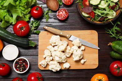 Photo of Healthy vegetarian food. Pieces of cauliflower, salad, peppercorns and vegetables on wooden table, flat lay