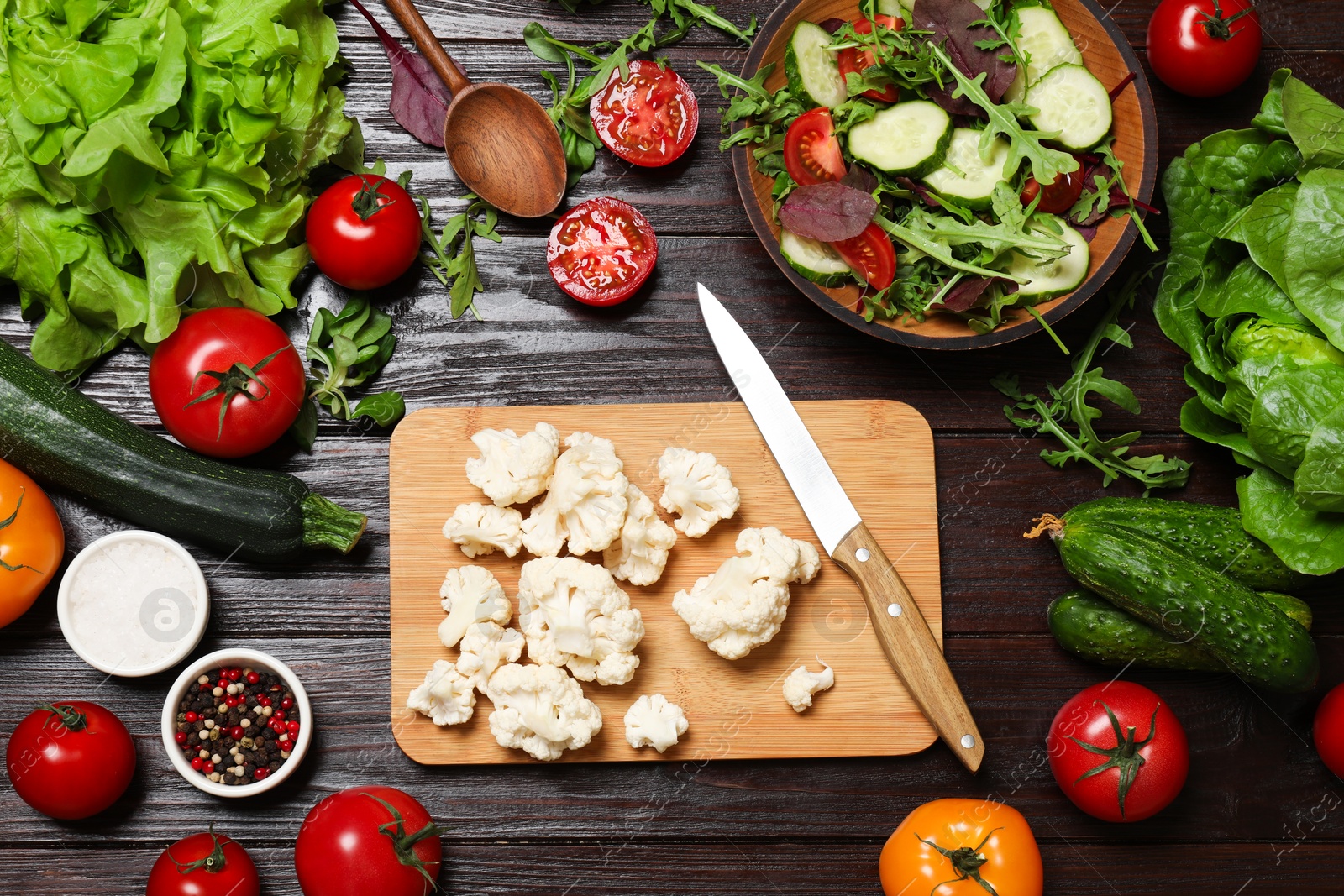 Photo of Healthy vegetarian food. Pieces of cauliflower, salad, peppercorns and vegetables on wooden table, flat lay