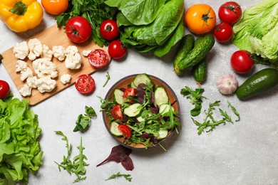 Photo of Healthy vegetarian food. Salad in bowl and vegetables on grey textured table, flat lay