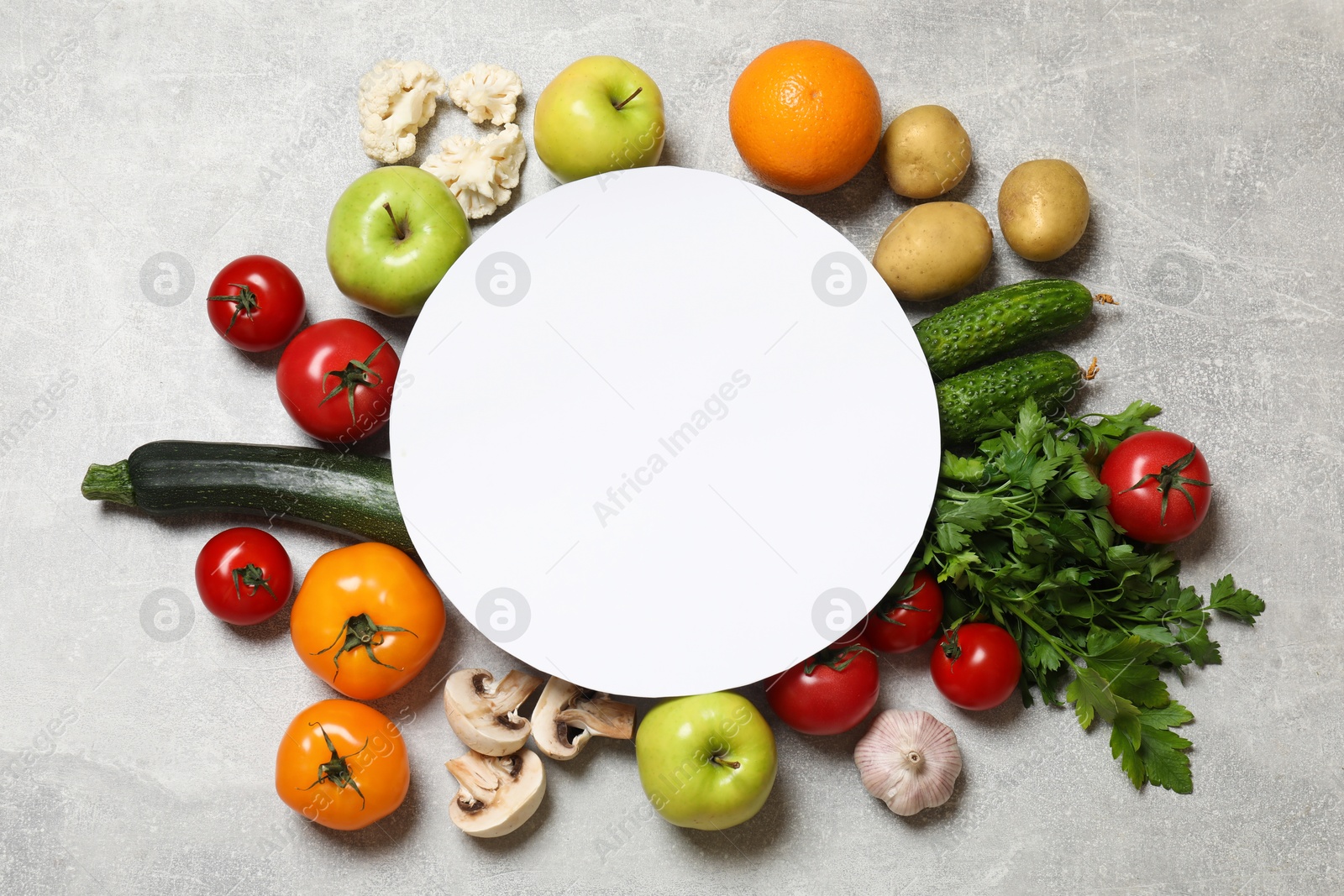 Photo of Healthy vegetarian food. Paper card surrounded by different vegetables and fruits on grey textured table, flat lay. Space for text