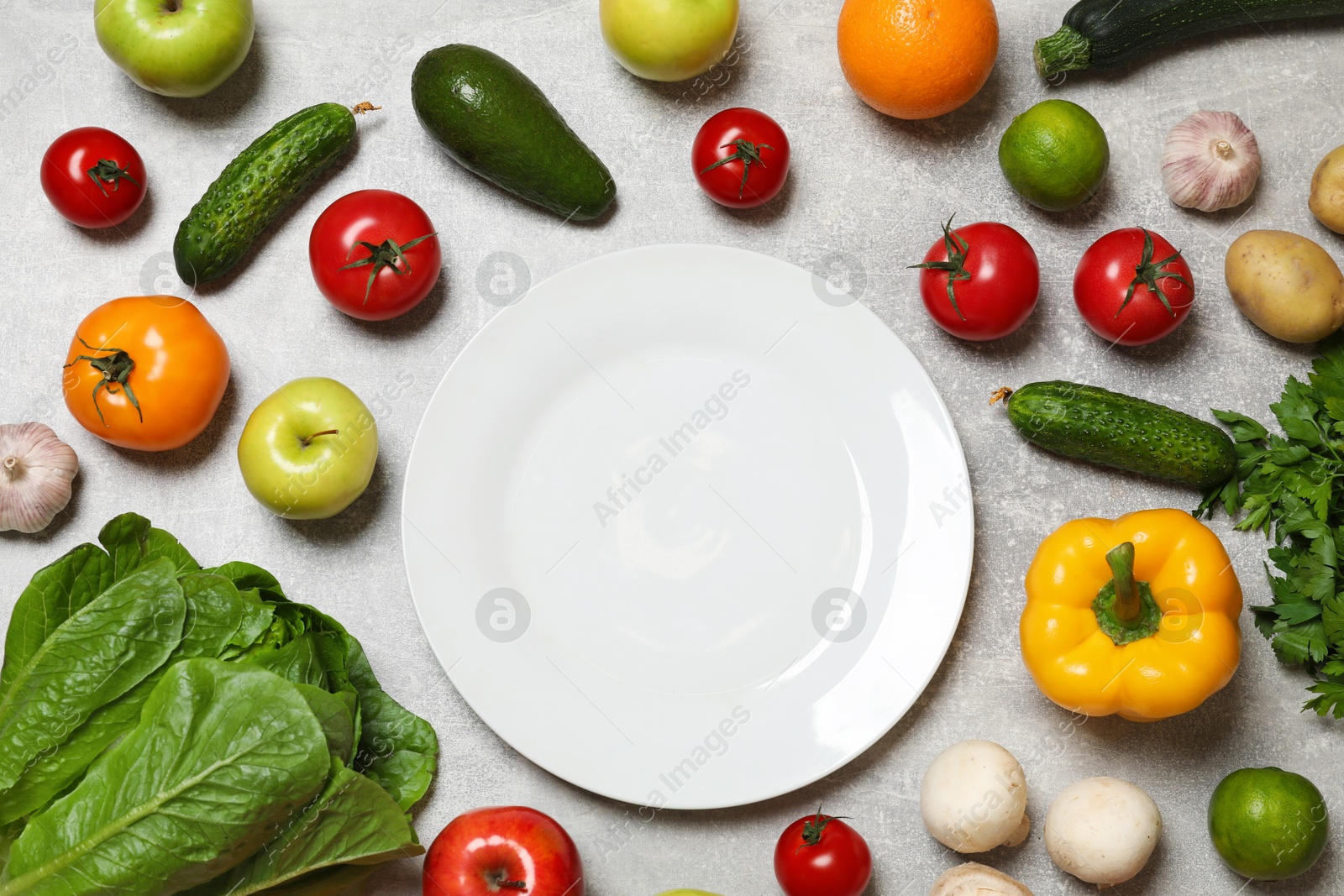 Photo of Healthy vegetarian food. Empty plate surrounded by different vegetables and fruits on grey textured table, flat lay