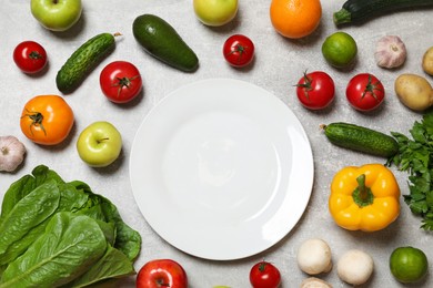 Photo of Healthy vegetarian food. Empty plate surrounded by different vegetables and fruits on grey textured table, flat lay