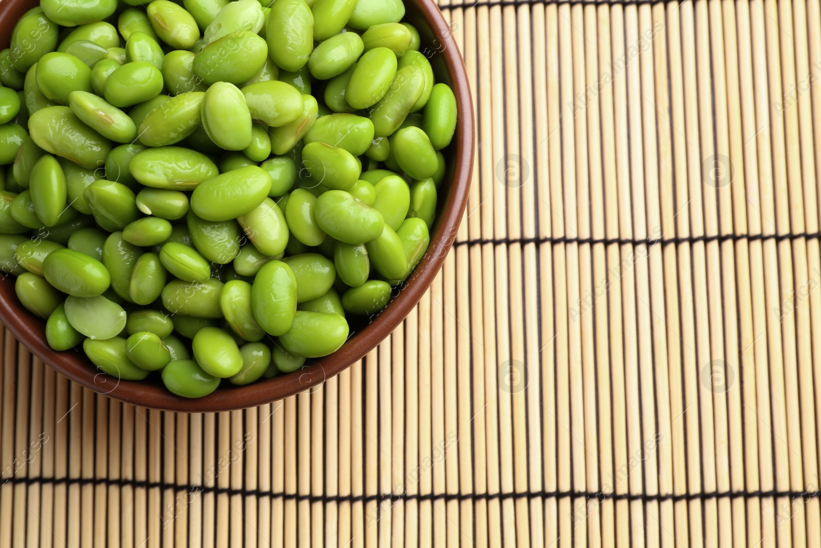 Photo of Raw green edamame soybeans on wicker mat, top view. Space for text