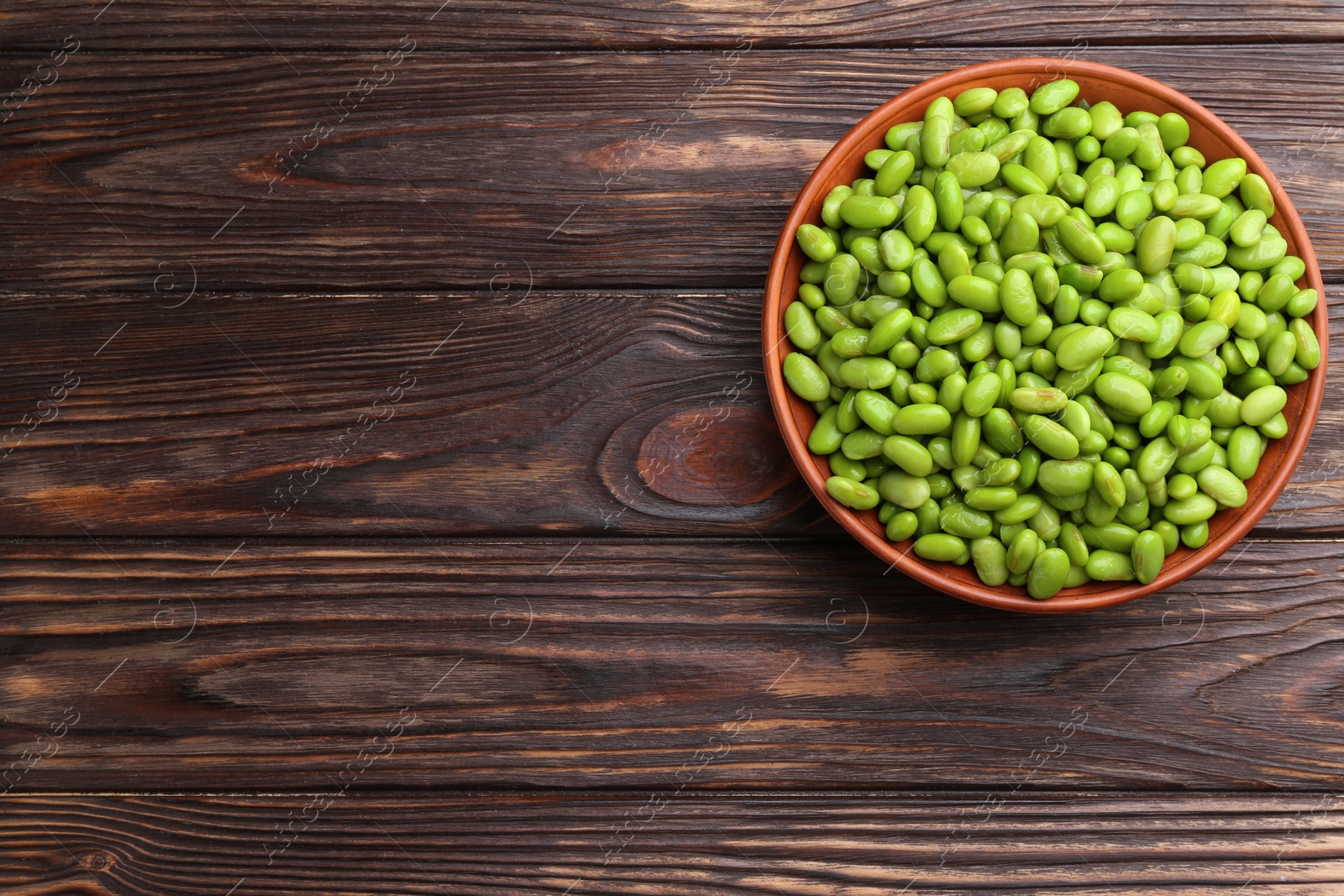 Photo of Raw green edamame soybeans in bowl on wooden table, top view. Space for text