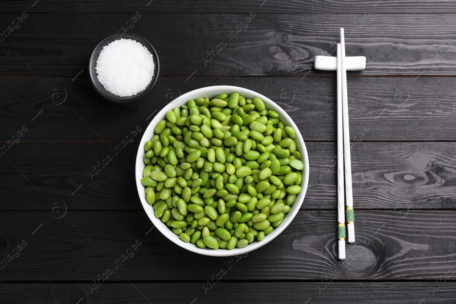 Photo of Raw green edamame soybeans, salt and chopsticks on wooden table, flat lay