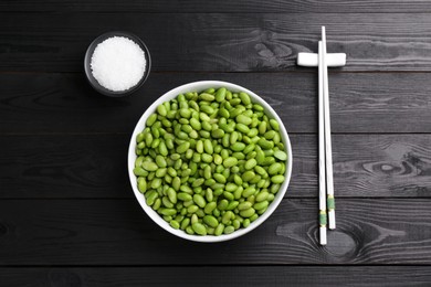 Raw green edamame soybeans, salt and chopsticks on wooden table, flat lay