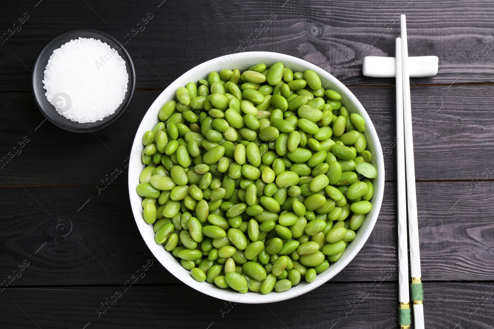 Photo of Raw green edamame soybeans, salt and chopsticks on wooden table, flat lay