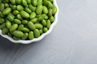 Photo of Fresh edamame soybeans in bowl on grey textured table, top view. Space for text