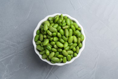 Photo of Fresh edamame soybeans in bowl on grey textured table, top view