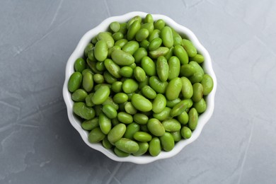 Fresh edamame soybeans in bowl on grey textured table, top view