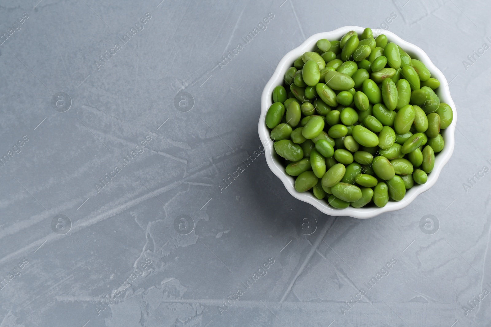 Photo of Fresh edamame soybeans in bowl on grey textured table, top view. Space for text