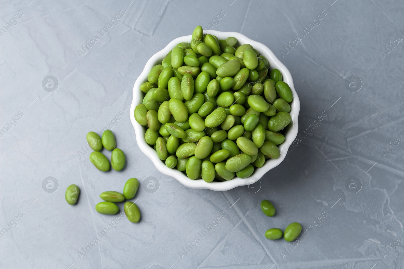 Photo of Fresh edamame soybeans in bowl on grey textured table, top view