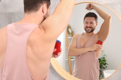 Smiling man applying solid deodorant near mirror at home, back view