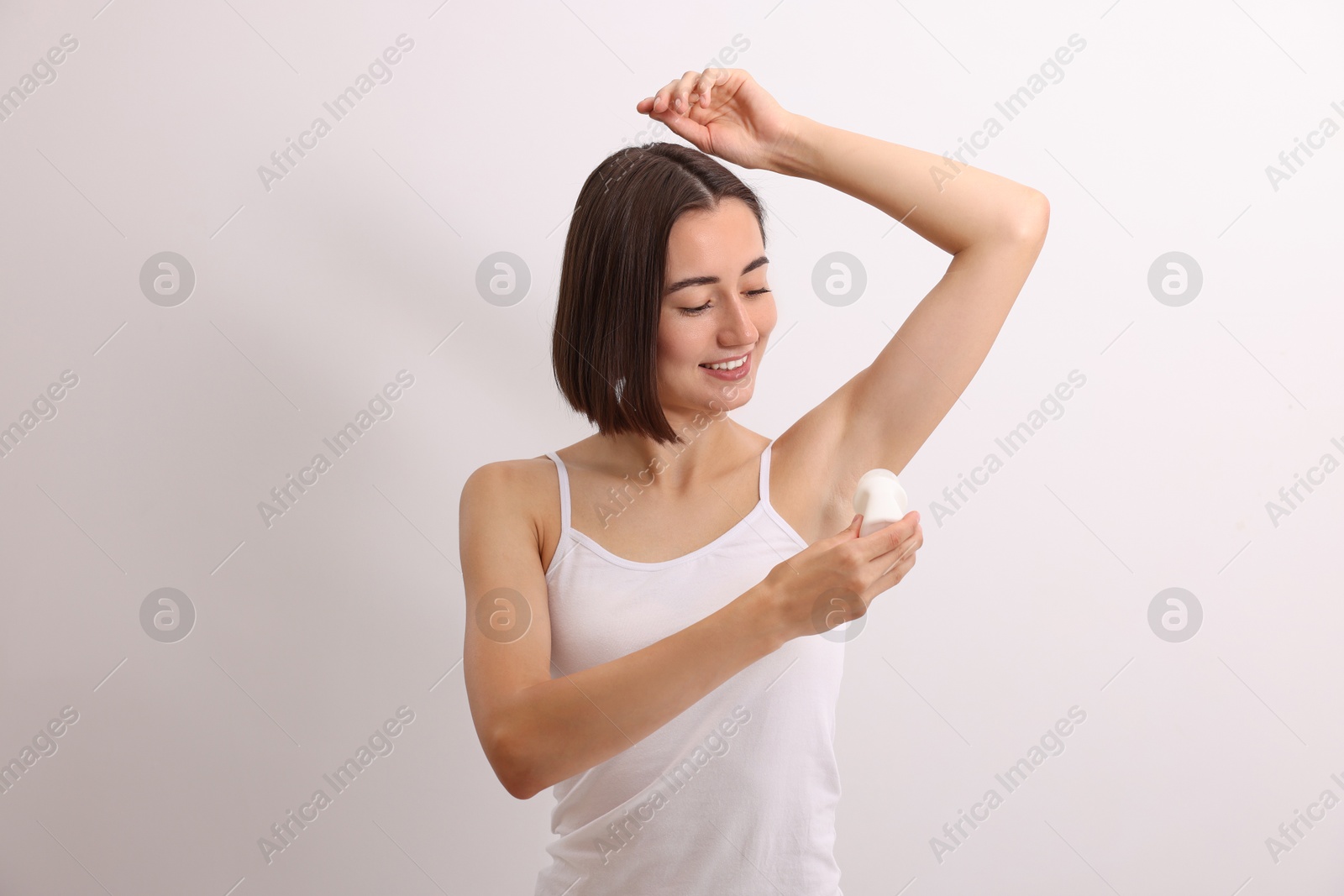 Photo of Smiling woman applying roll-on deodorant on white background