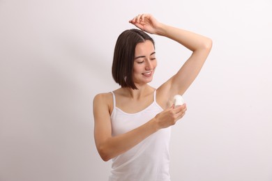 Photo of Smiling woman applying roll-on deodorant on white background