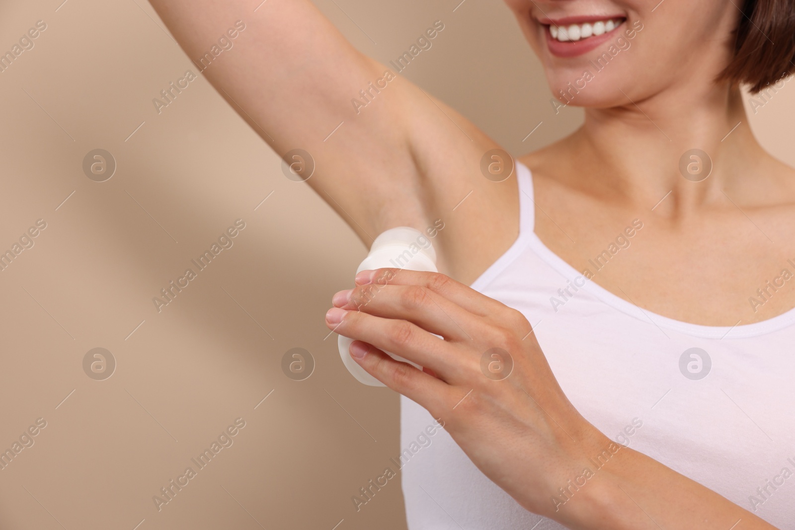 Photo of Smiling woman applying roll-on deodorant on beige background, closeup