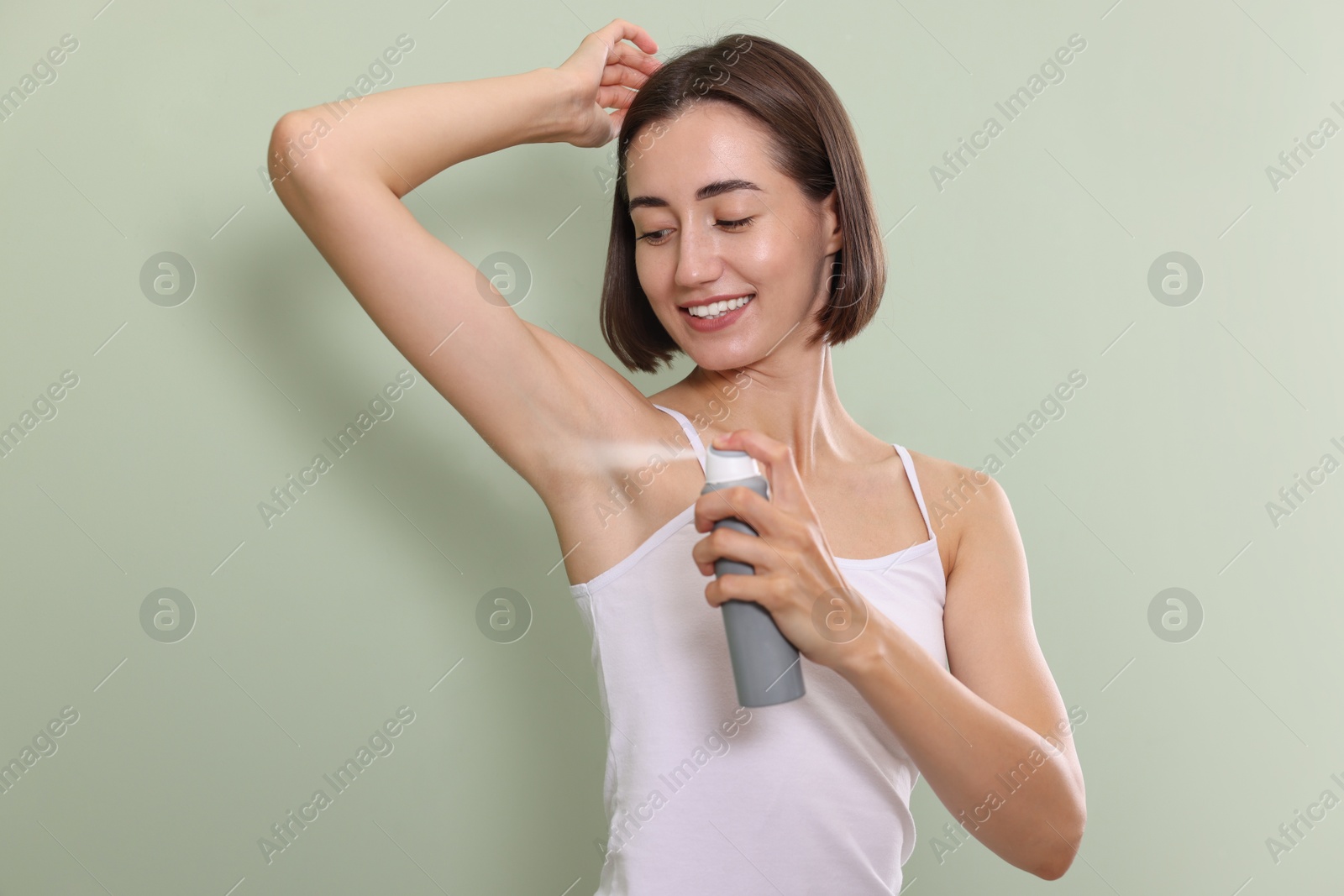 Photo of Smiling woman applying spray deodorant on green background