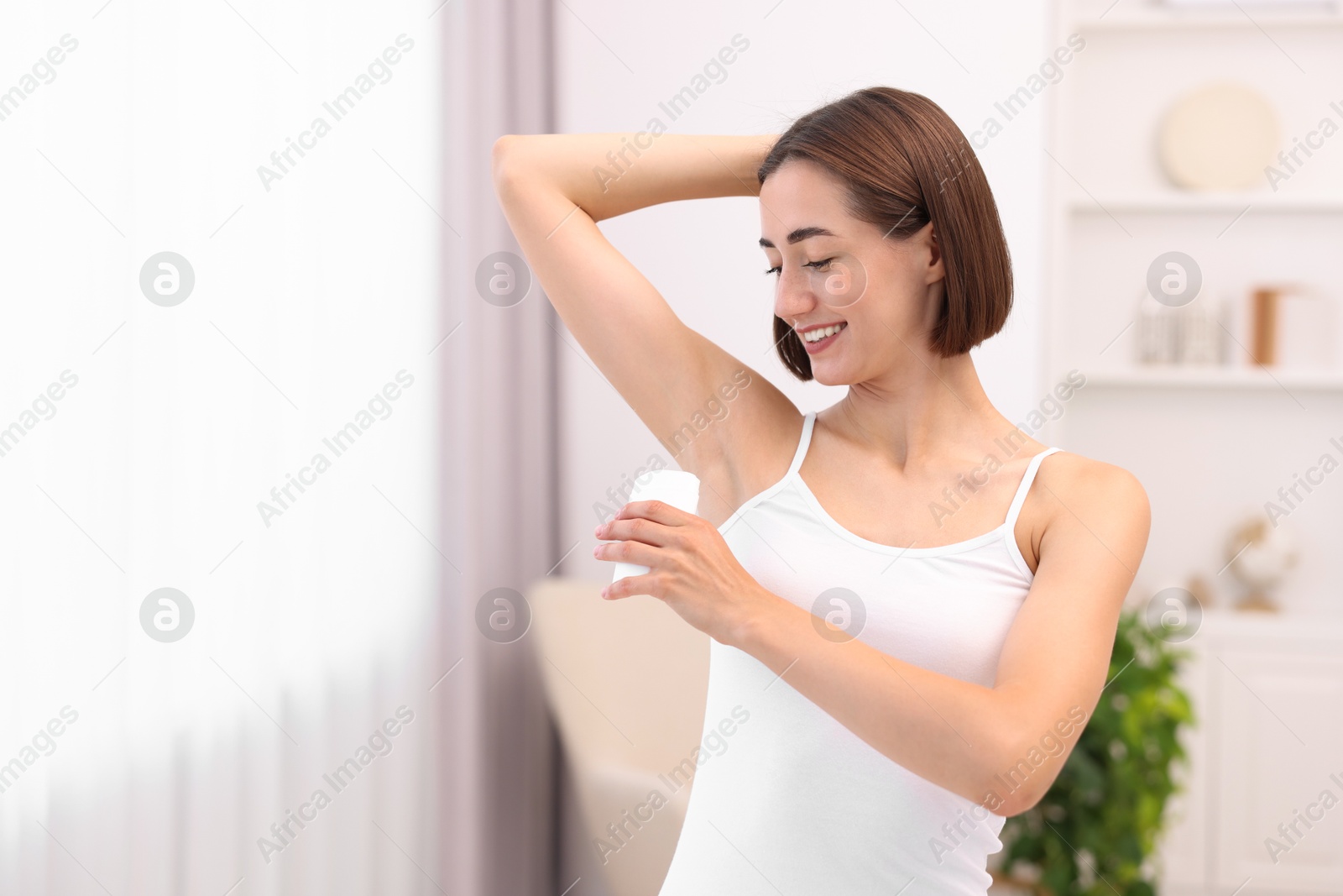 Photo of Smiling woman applying solid deodorant at home. Space for text