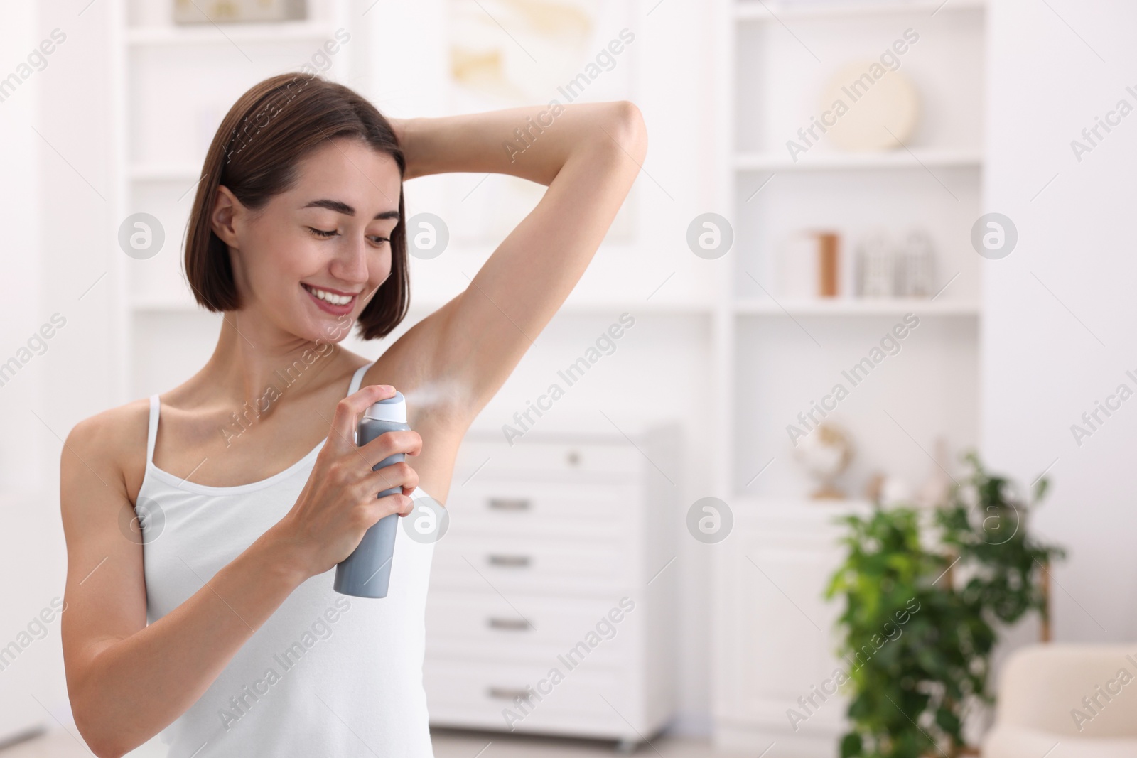 Photo of Smiling woman applying spray deodorant at home. Space for text