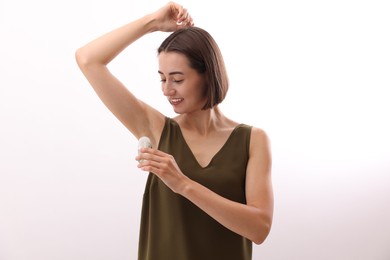 Photo of Smiling woman applying roll-on deodorant on white background