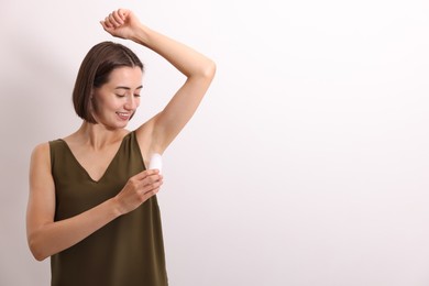 Photo of Smiling woman applying roll-on deodorant on white background. Space for text