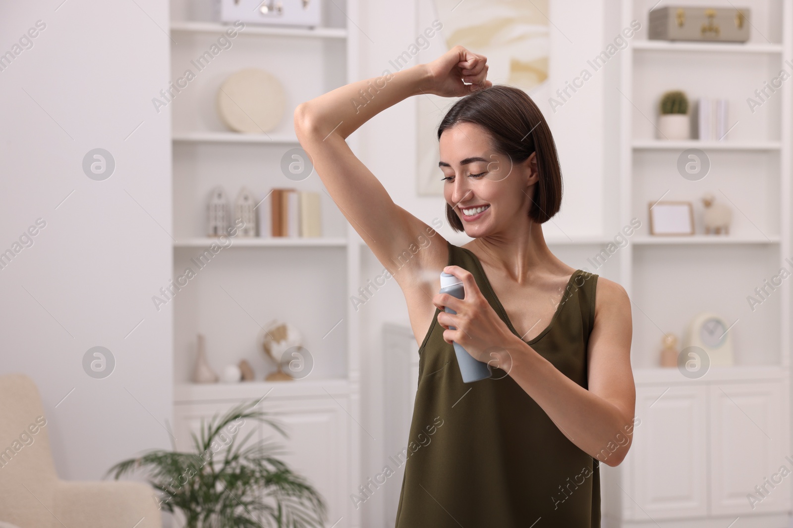 Photo of Smiling woman applying spray deodorant at home. Space for text