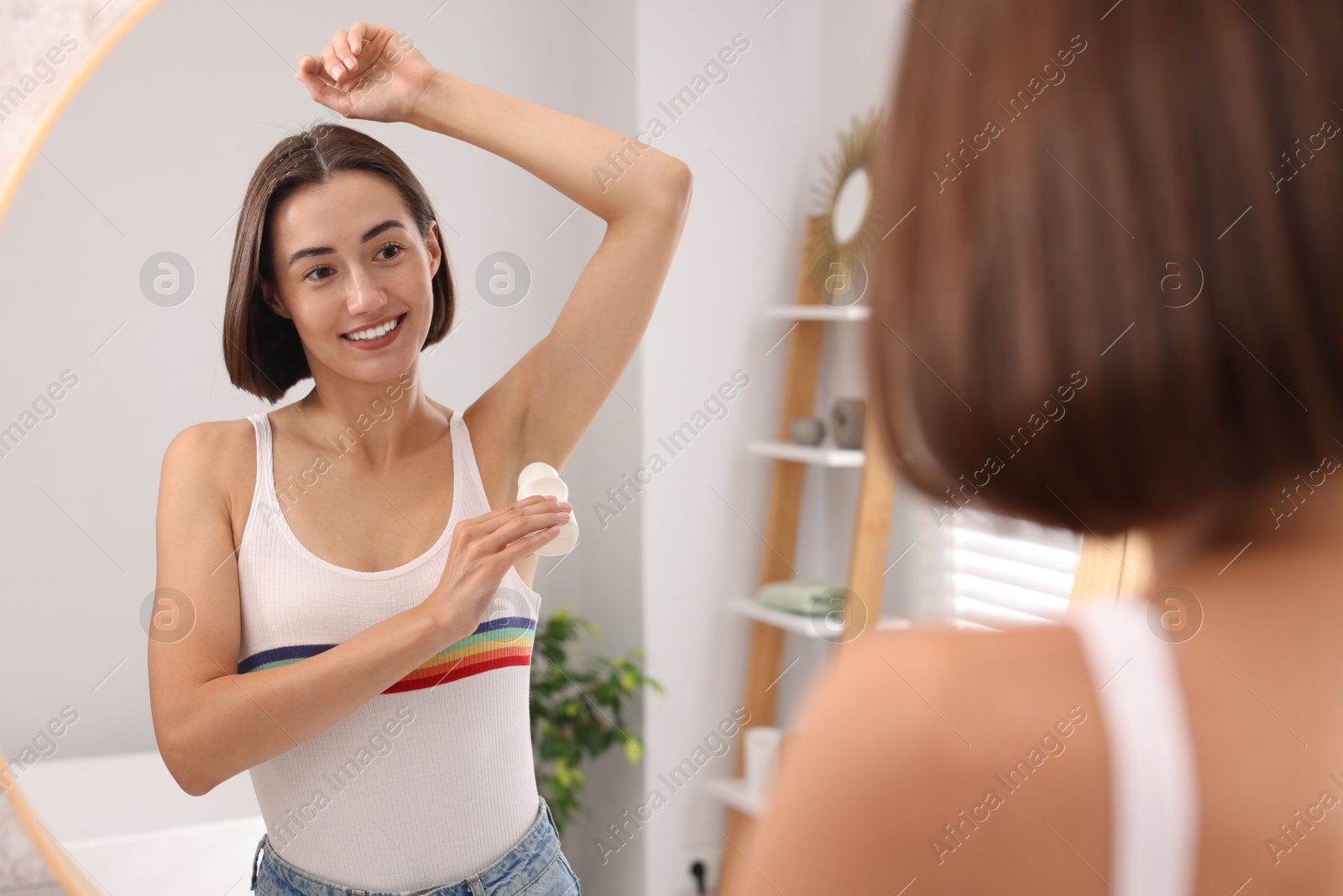 Photo of Smiling woman applying roll-on deodorant near mirror at home