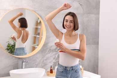 Photo of Smiling woman applying roll-on deodorant in bathroom